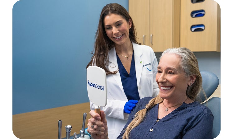 A woman is smiling while looking at her teeth in a mirror