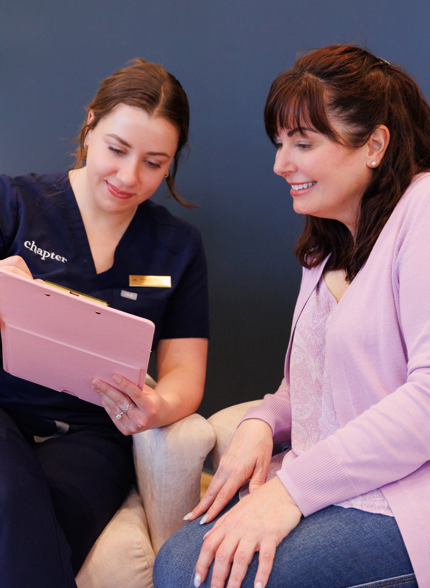 A client meets with an aesthetic provider at Chapter Aesthetics Studio for a personalized consultation. The specialist reviews treatment options on a tablet while the client listens and smiles, highlighting the studio’s warm, friendly, and professional approach to customized aesthetic care.