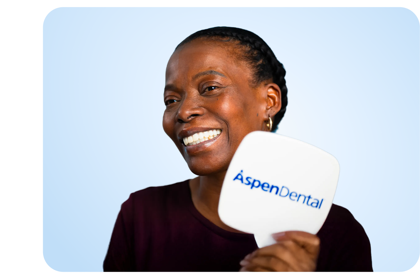 A smiling patient holds an Aspen Dental mirror displayed on a light blue background.