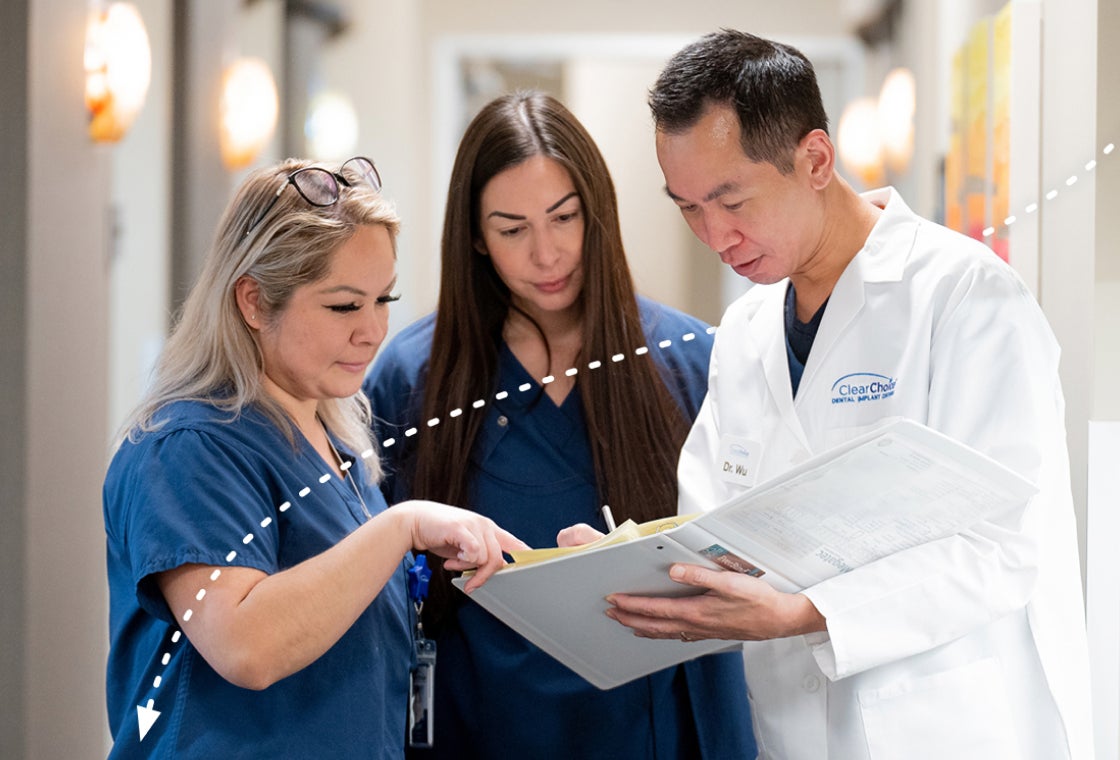 ClearChoice dental team members collaborating and reviewing a patient’s treatment plan together in a clinic hallway.