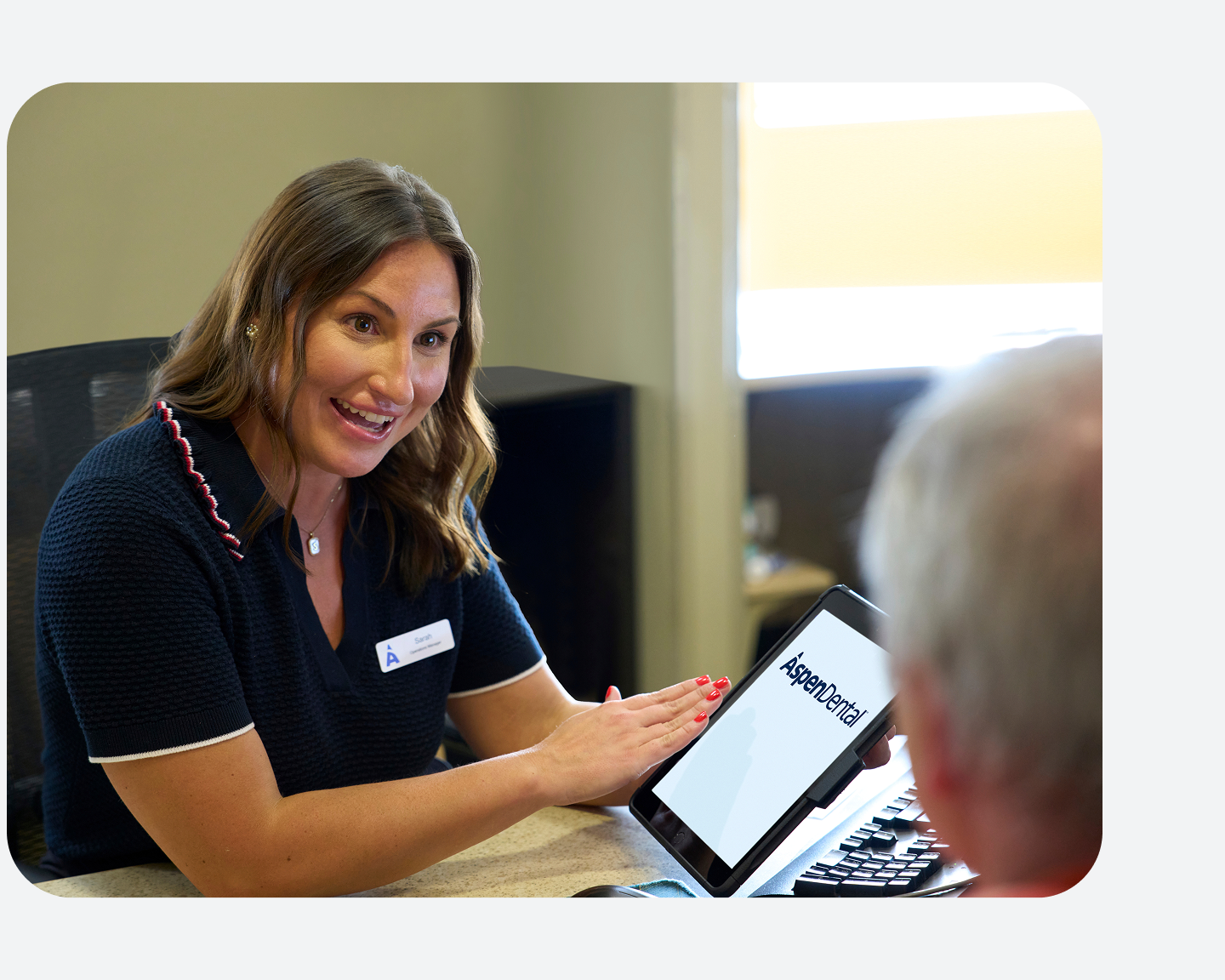 An Aspen Dental team member smiles while reviewing information on a tablet with a patient during a consultation at the front desk.