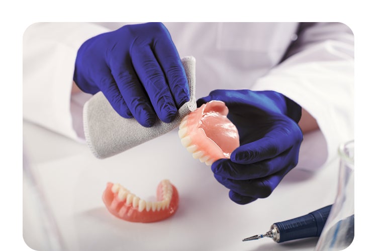 A person wearing blue gloves is working on a denture