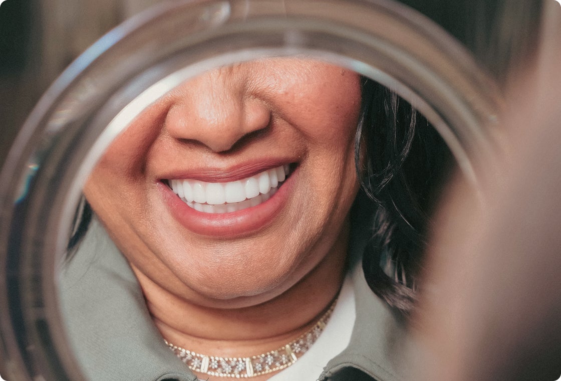 A woman smiling into a mirror as she admires her new dental implants.