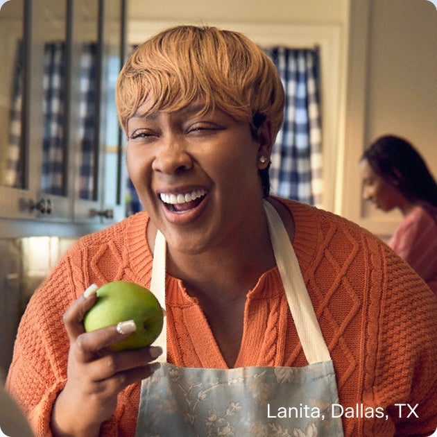 Lanita from Dallas, TX smiling and holding a green apple after dental implant treatment, demonstrating strong bite function and the everyday benefits of full mouth dental implants.