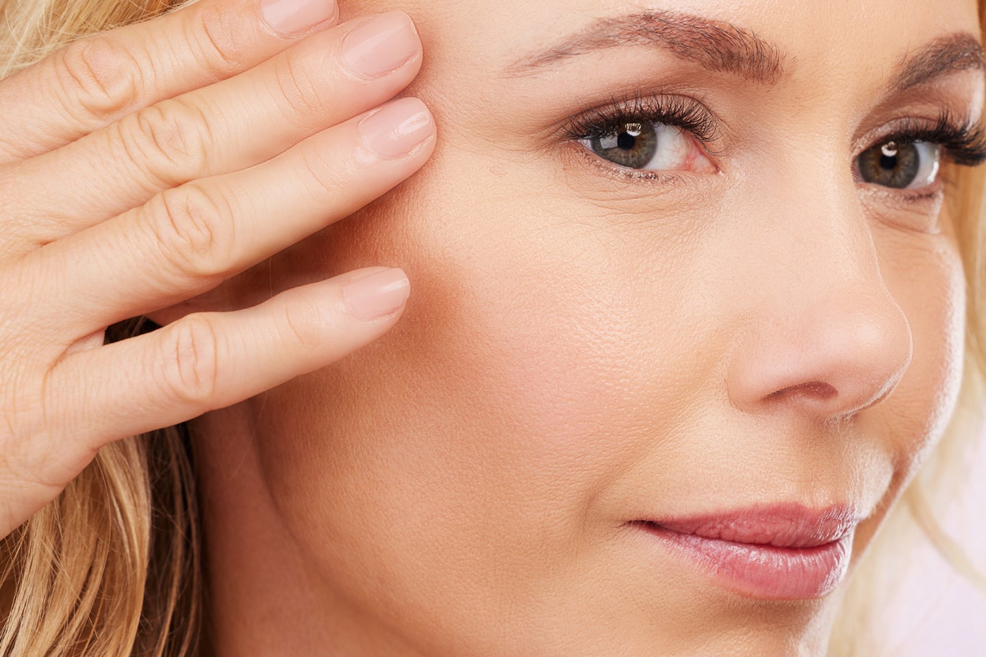 Closeup of a woman's face, showing her smooth skin, with her hand gently touching her temple