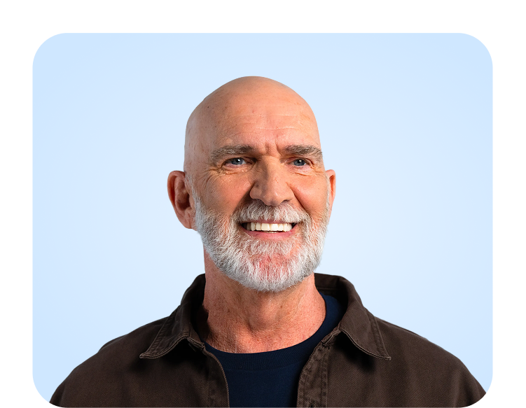 A smiling male patient with a neatly trimmed white beard poses against a light blue background, showcasing a healthy, confident smile