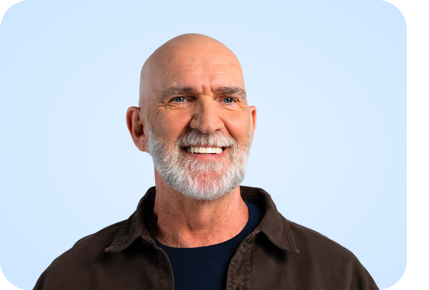 A smiling male patient with a neatly trimmed white beard poses against a light blue background, showcasing a healthy, confident smile.