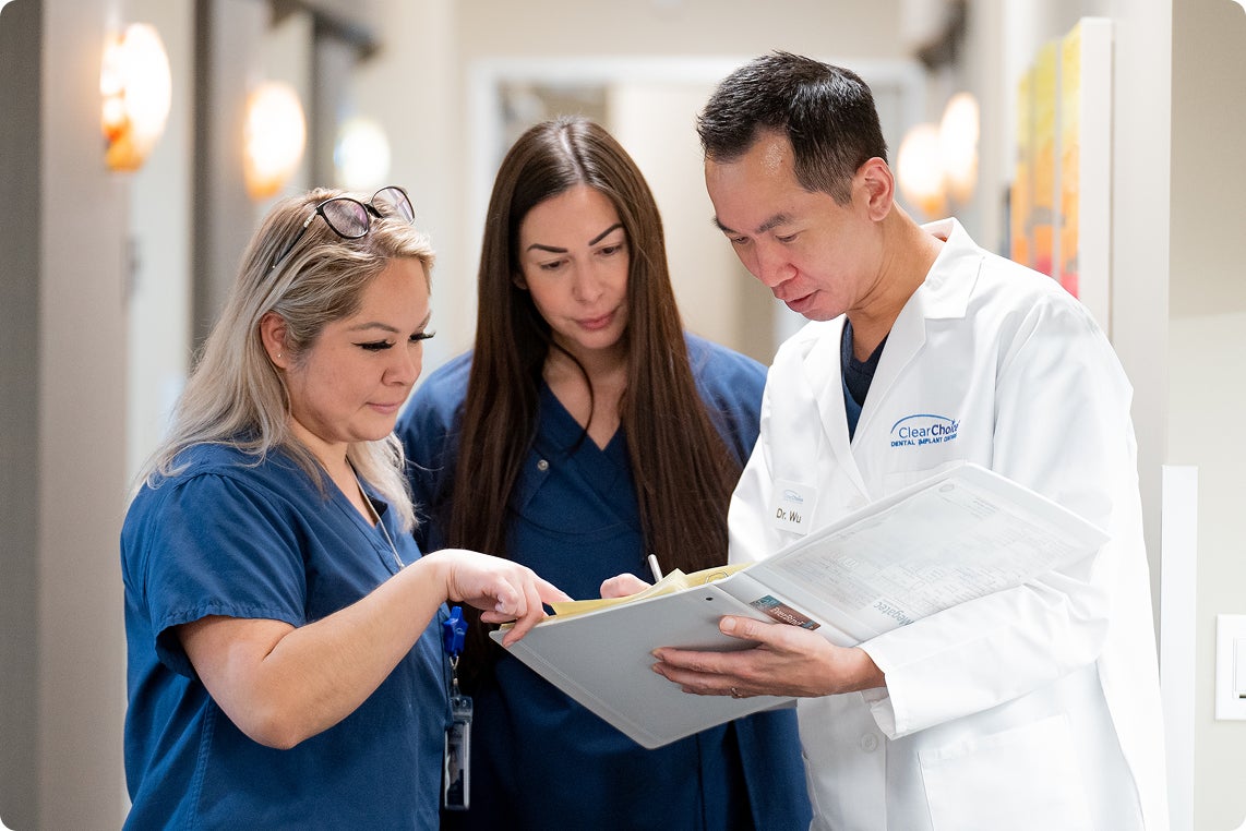 ClearChoice dental care team reviews a patient chart together in a clinic hallway, reflecting collaboration and precision in dental implant treatment planning.