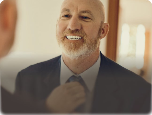Man smiling in a suit adjusting his tie with overlay text: “Ready to upgrade? Go from dentures to implants.”