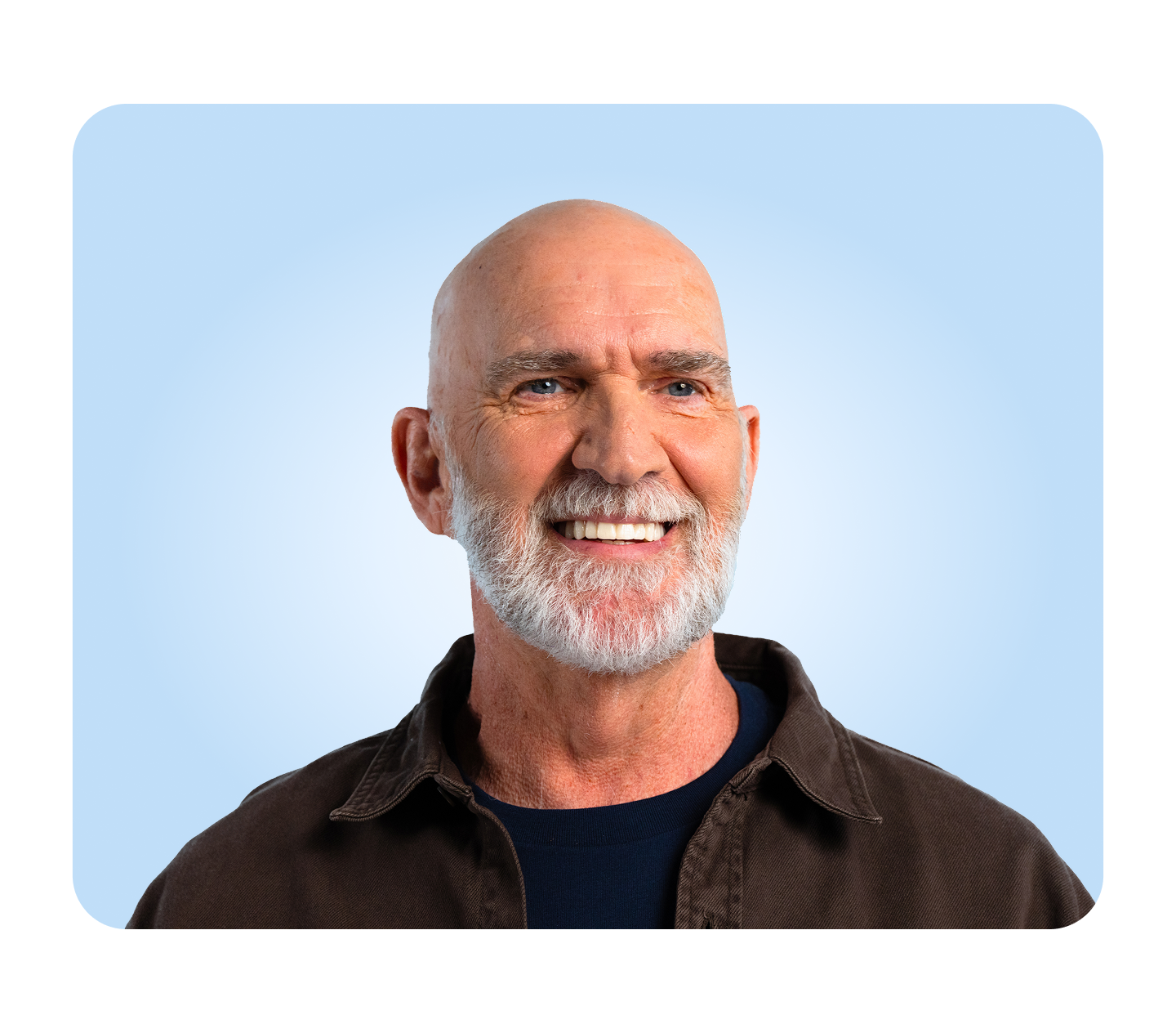 A smiling male patient with a white beard looks confidently toward the side, standing against a light blue background.