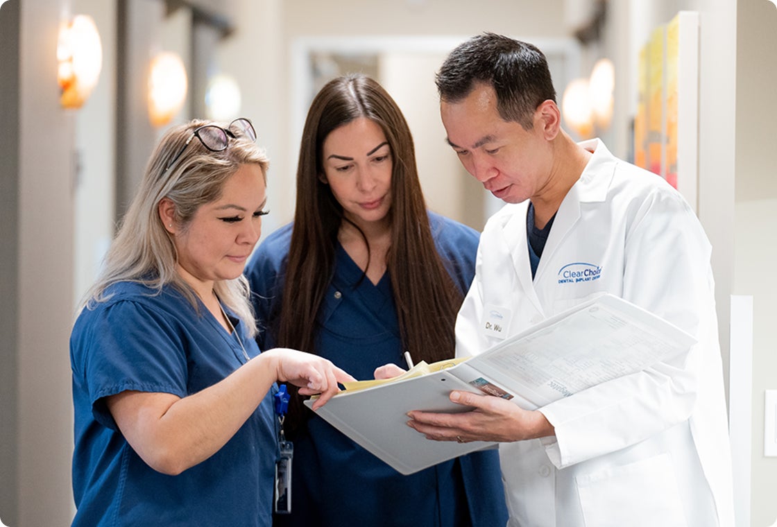 ClearChoice dental care team reviews a patient chart together in a clinic hallway, reflecting collaboration and precision in dental implant treatment planning.