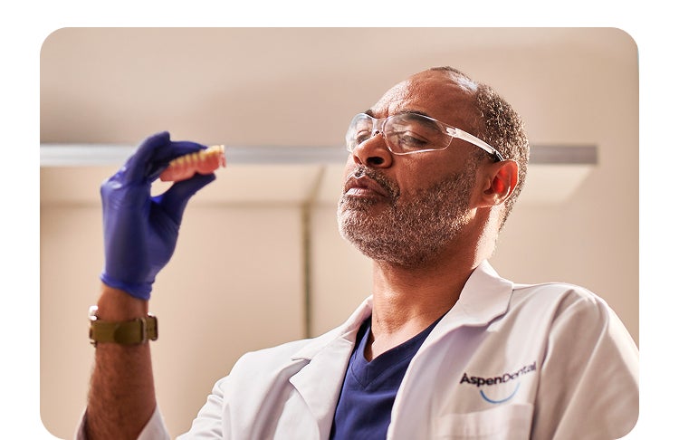 A man in a lab coat is holding a tooth in his hand