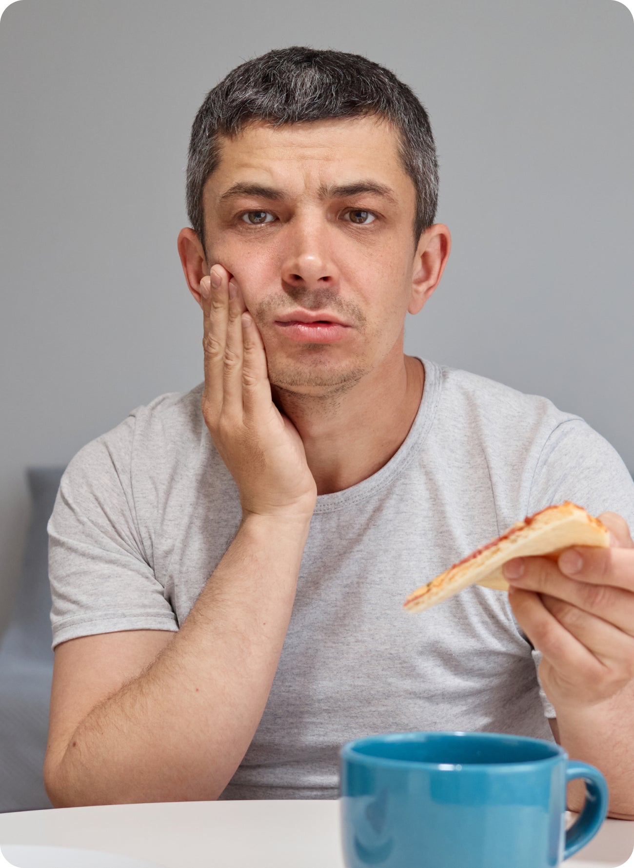 Man holding his cheek while eating, suggesting gum pain or discomfort during meals.