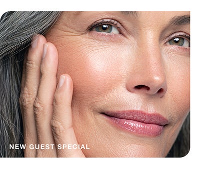 A smiling woman with radiant, mature skin gently touches her face, advertising a "new guest special."