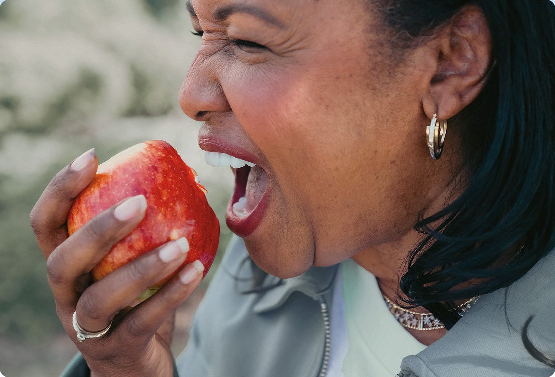 A female patient from ClearChoice, enjoying an apple post-recovery after her dental implants treatment.