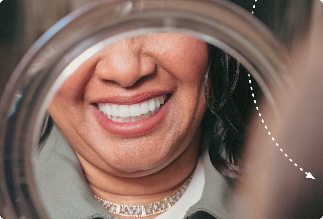 A patient smiling while looking at her new teeth in a handheld mirror, reflecting the results of her ClearChoice dental implant treatment.