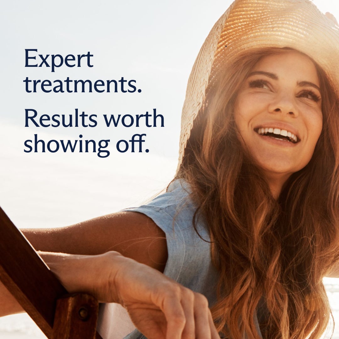 A smiling woman holding onto a sunhat on a sunny beach, overlaid with text which reads "Expert treatments. Results worth showing off."