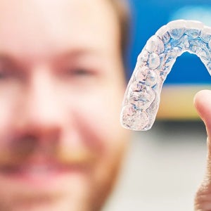 Close-up of a clear aligner held in hand, representing treatment and candidacy for clear aligners with Motto