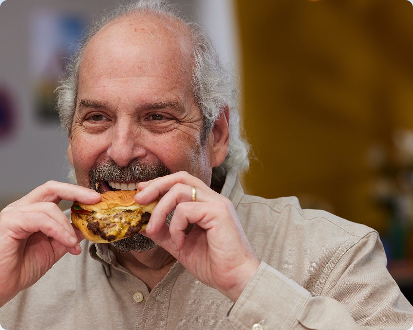 A ClearChoice patient enjoying a burger again after following post-surgery diets and healing completely after his dental implants procedure.