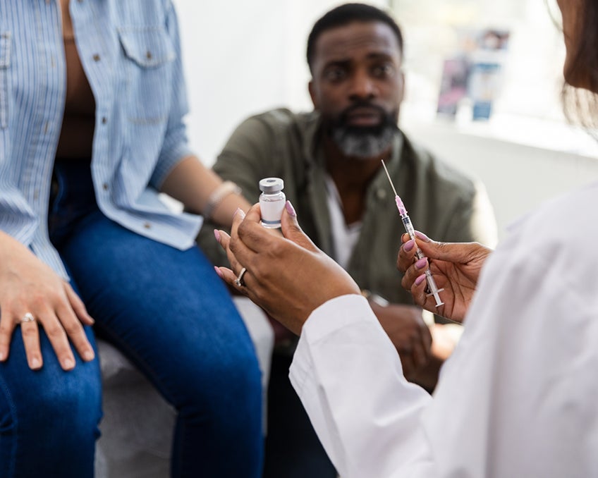 A provider gives a patient a cortisone injection with a family member watching in the background.
