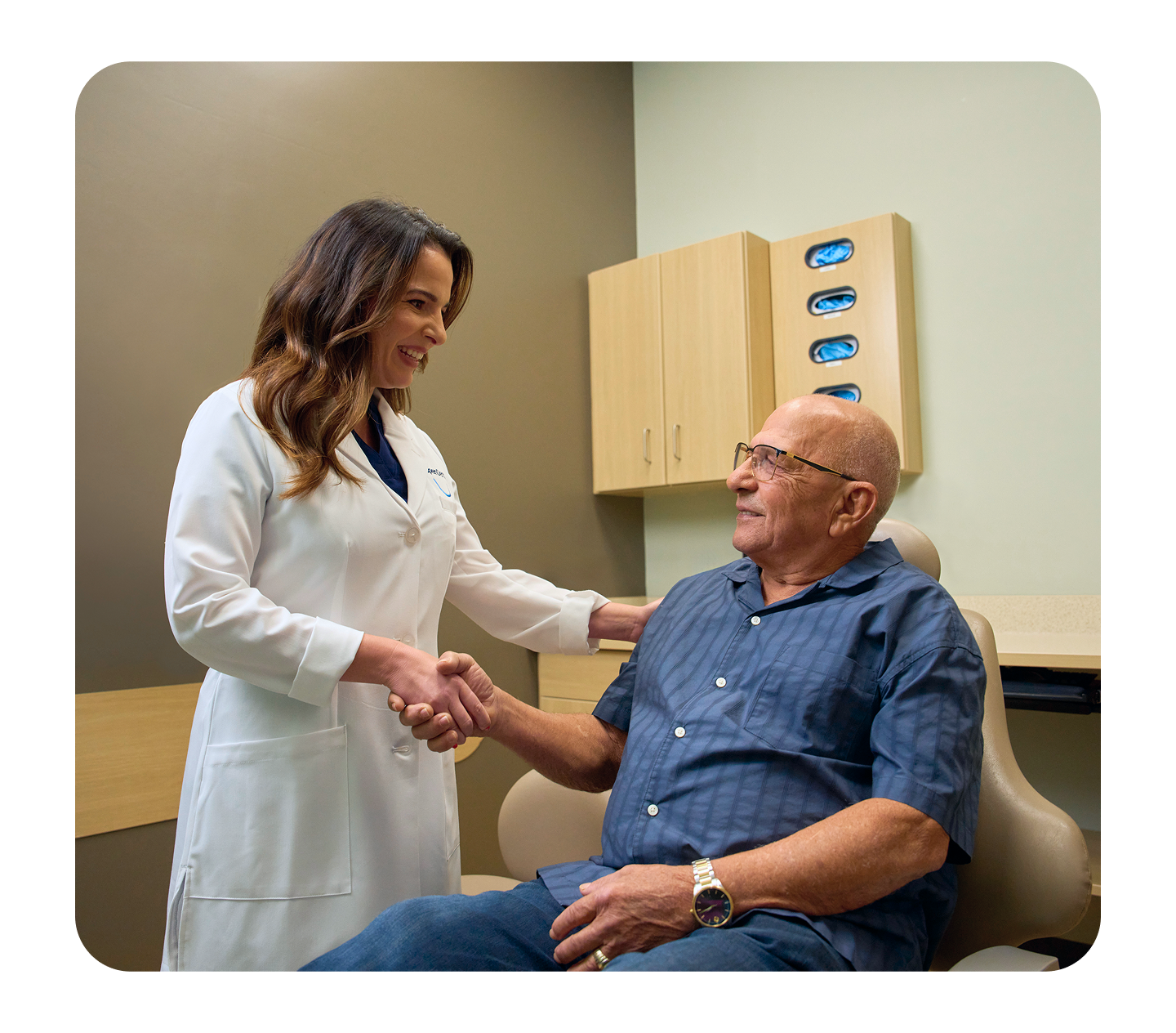 A dentist warmly greets an older male patient with a handshake during a dental consultation in a modern clinic exam room.