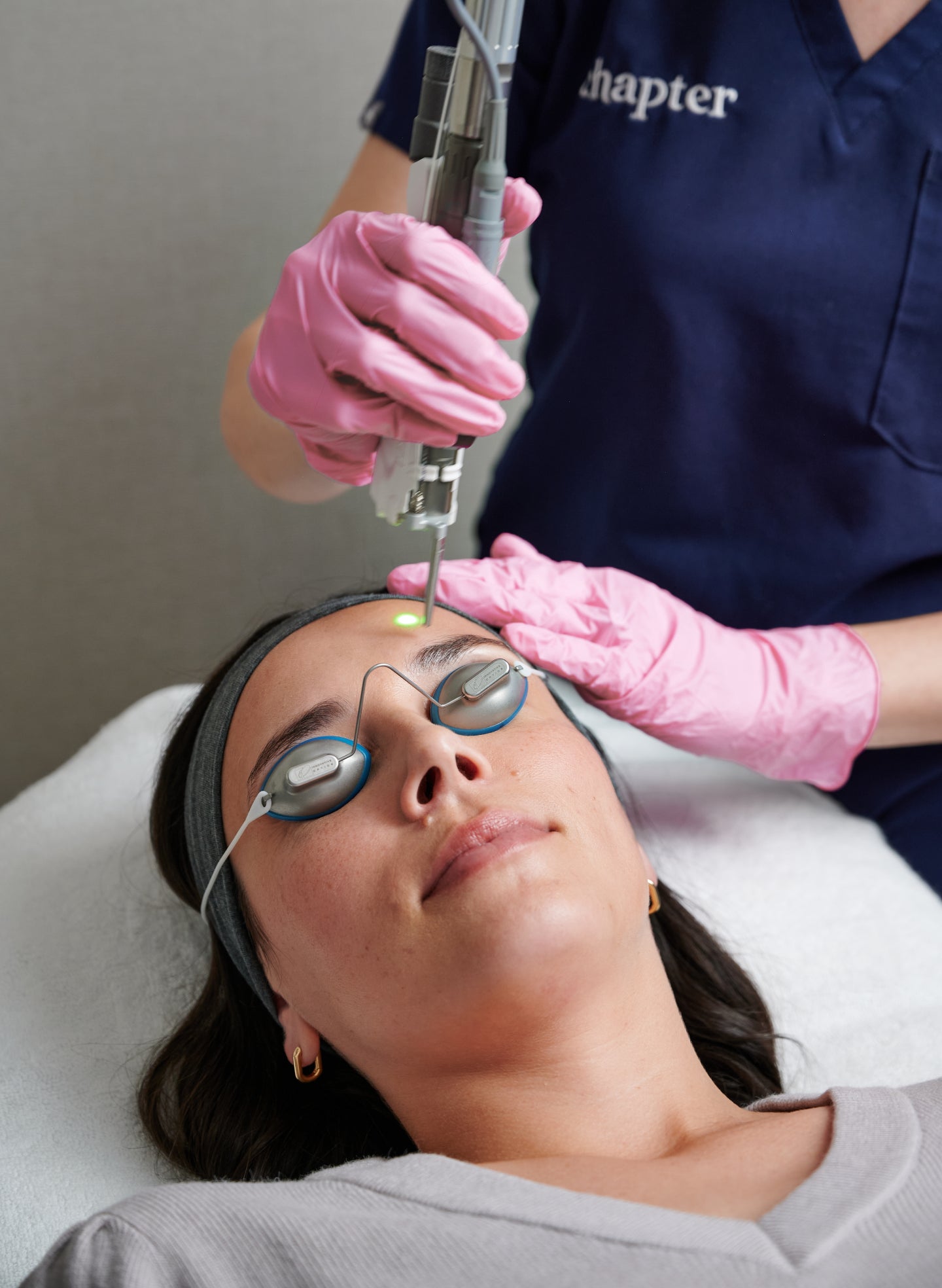 A client receives a professional facial laser treatment at Chapter Aesthetics Studio. The aesthetic provider, wearing pink gloves and protective eyewear, uses an advanced laser device while the client lies comfortably with eye shields in place, highlighting the studio’s expertise in skin rejuvenation and corrective laser services.