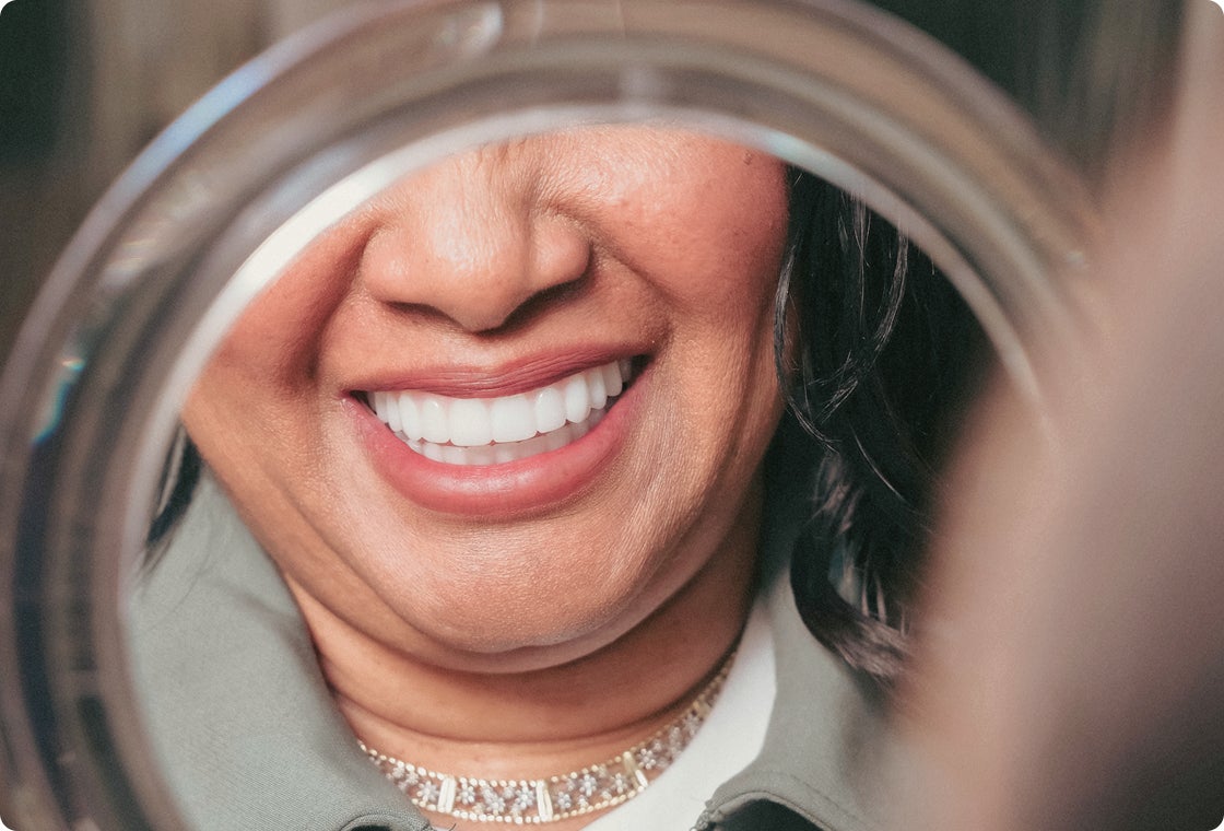 Close-up of a woman admiring her new smile in a mirror after dental implant treatment, showcasing the natural look and confidence dental implants can help restore.