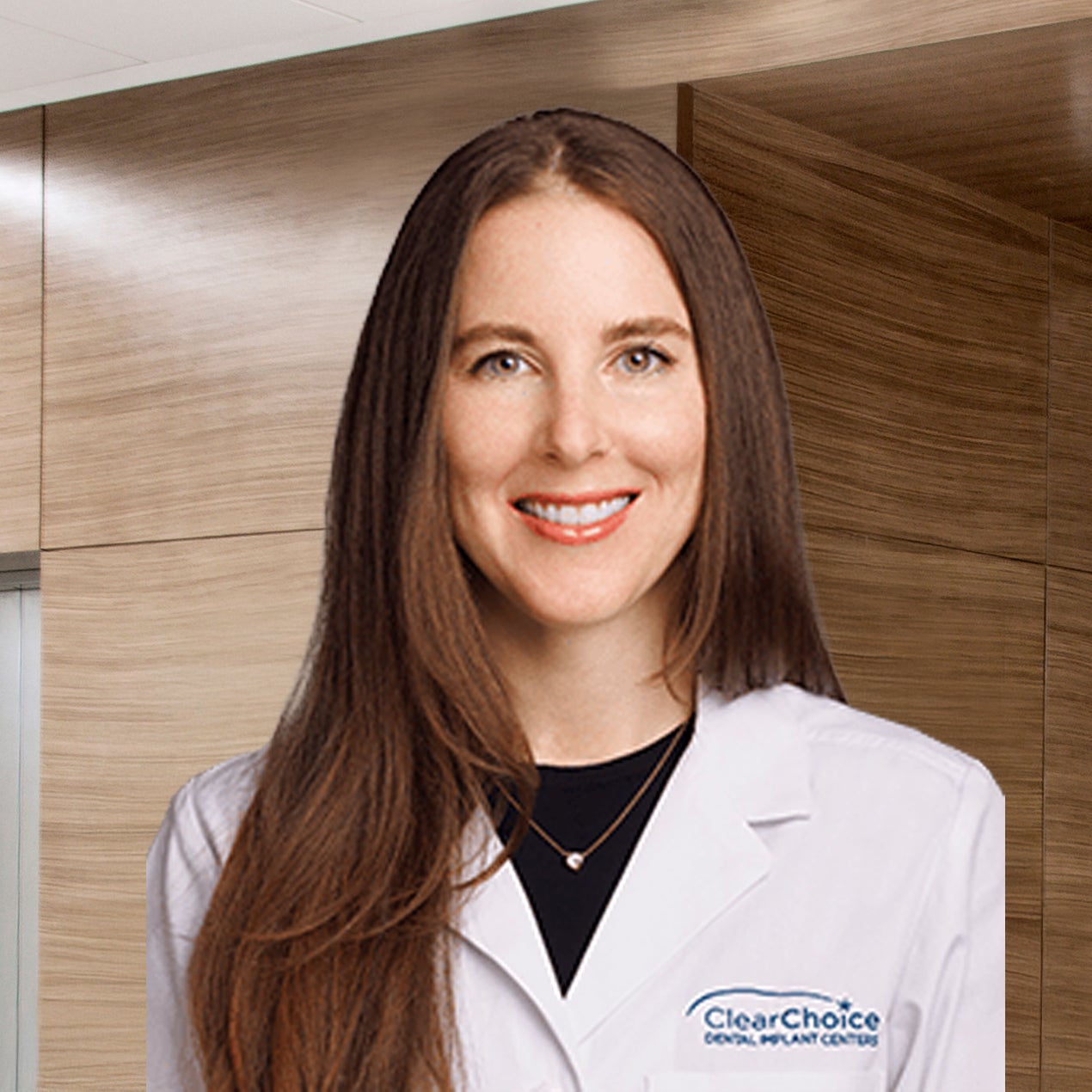 Dr. Kristin Hutkin in a white ClearChoice coat smiling in front of a brown wood office wall