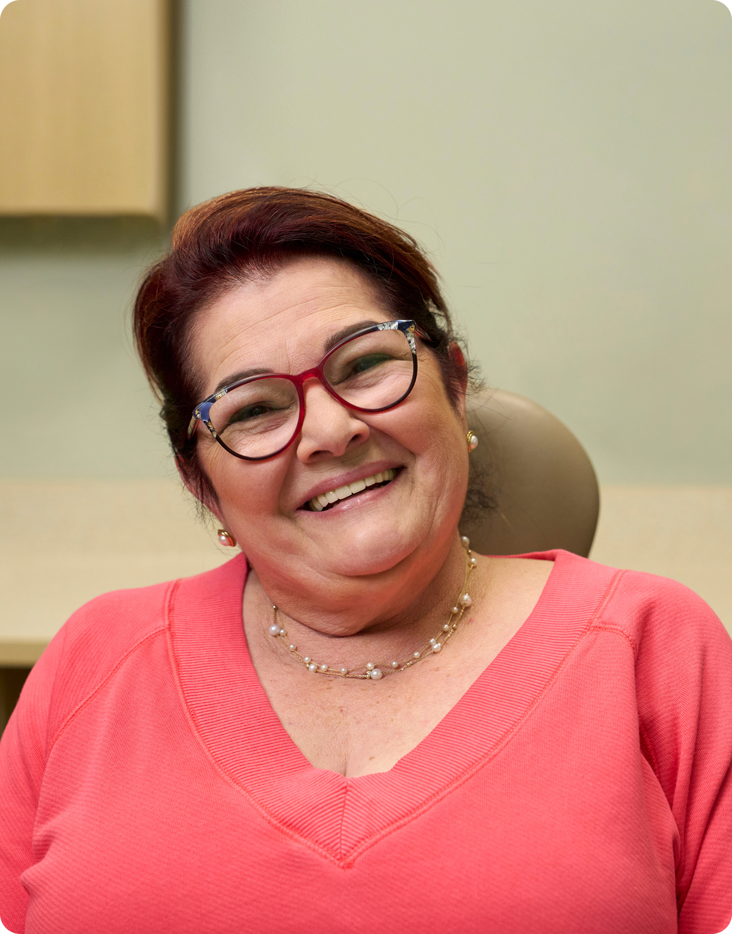Smiling older woman sitting in a dental office, representing how oral health impacts overall health.