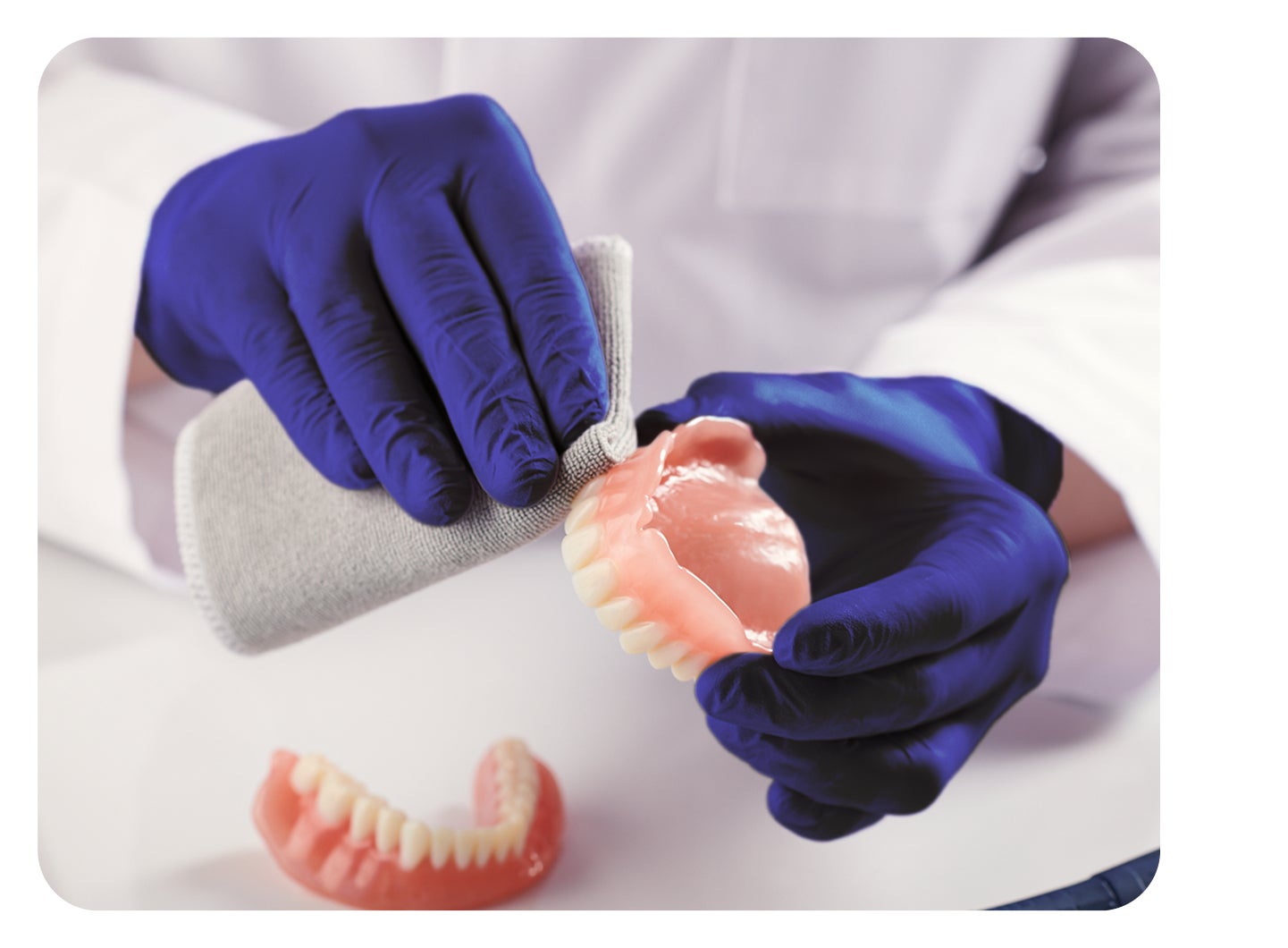 A person wearing blue gloves is working on a denture