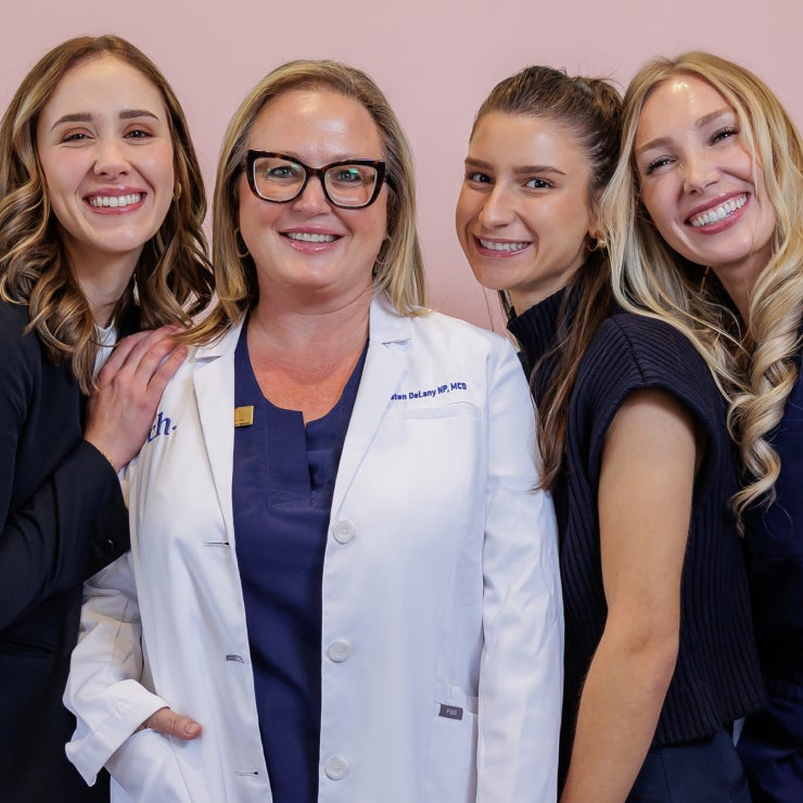 A smiling team of four professional women, one in a lab coat