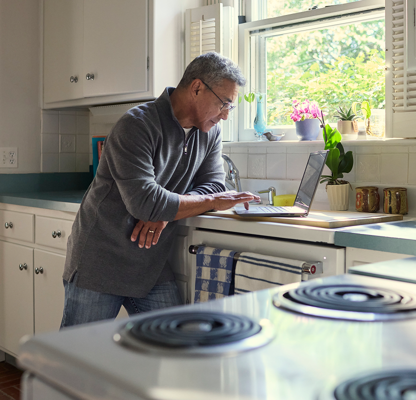 Older adult man using a laptop at home, researching or managing dental care information.