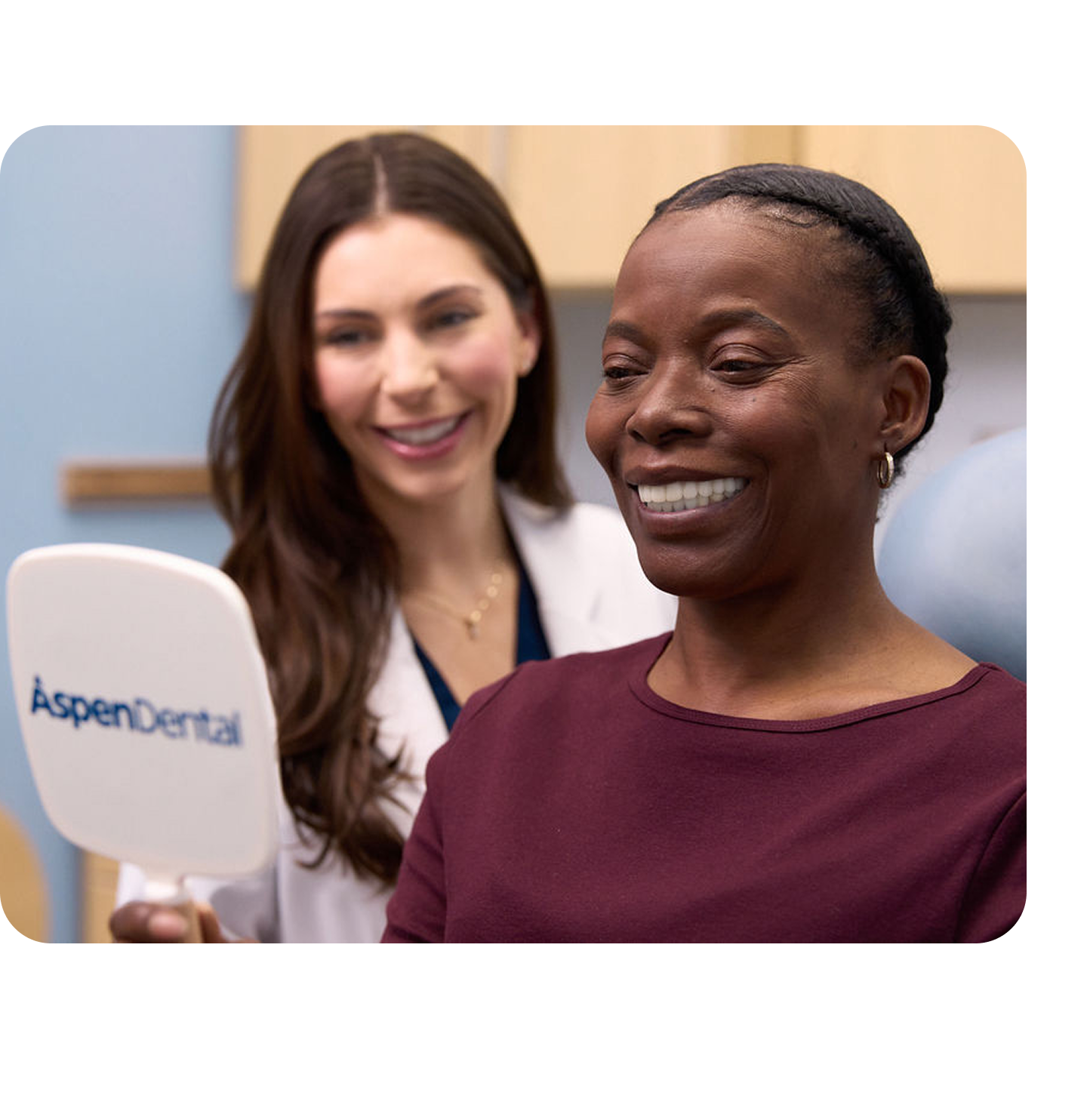 An Aspen Dental doctor in a white coat and blue gloves is smiling while having a discussion with a woman sitting in the dental chair.
