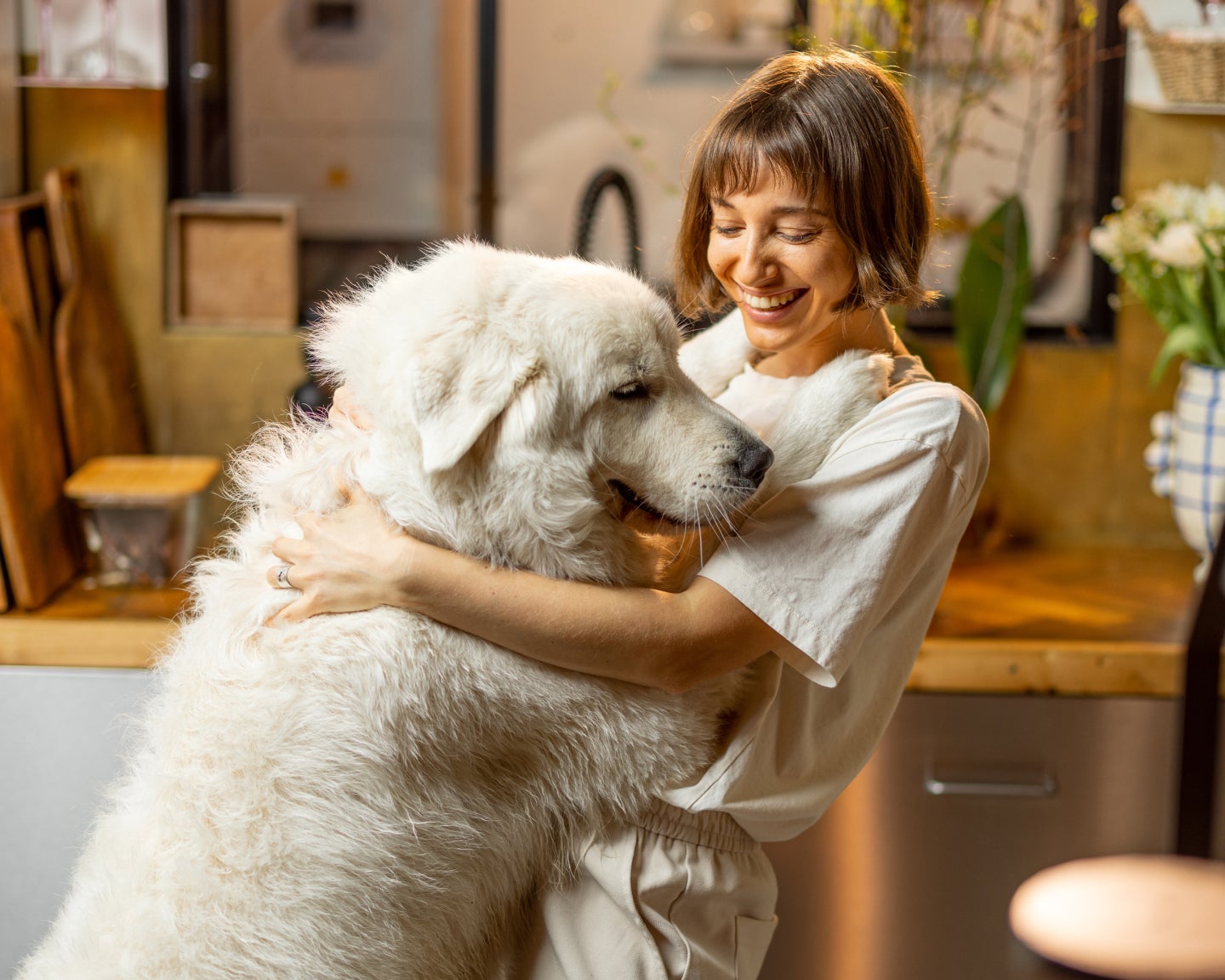 A pet parent dances with their Great Pyrenees in a kitchen with warm lighting.