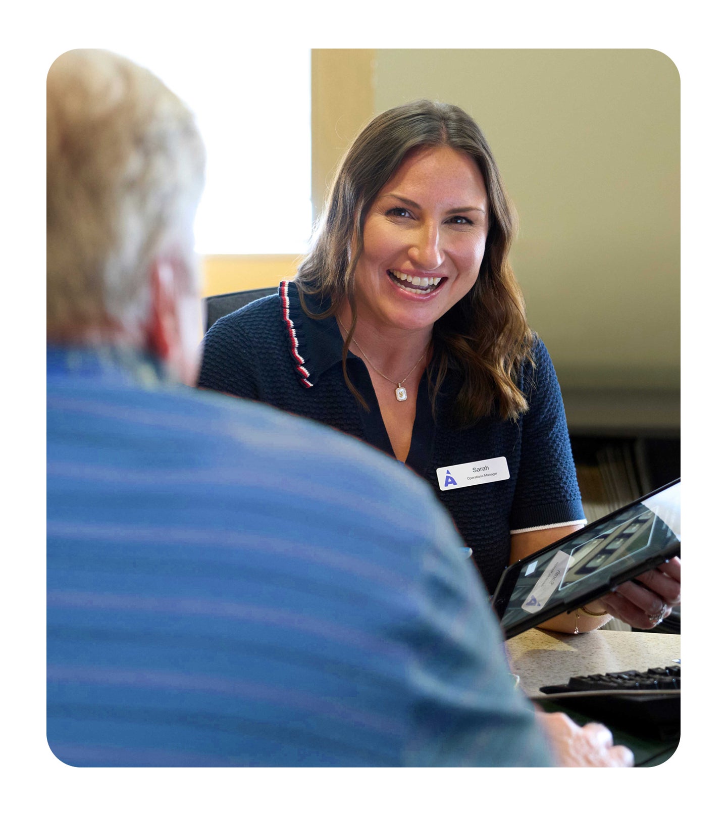 An Aspen Dental team member smiles warmly while speaking with a patient across the desk, holding a tablet during a consultation.