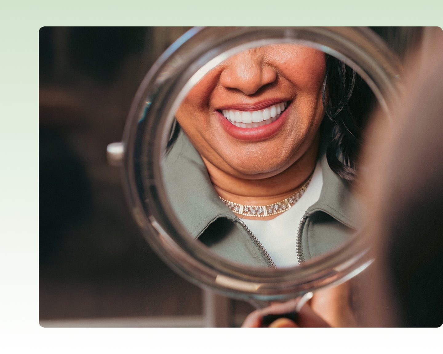 A ClearChoice patient smiling into a hand held mirror with her new dental implants, which she was able to receive $5,000 off for with the exclusive Insurance Assurance discount.