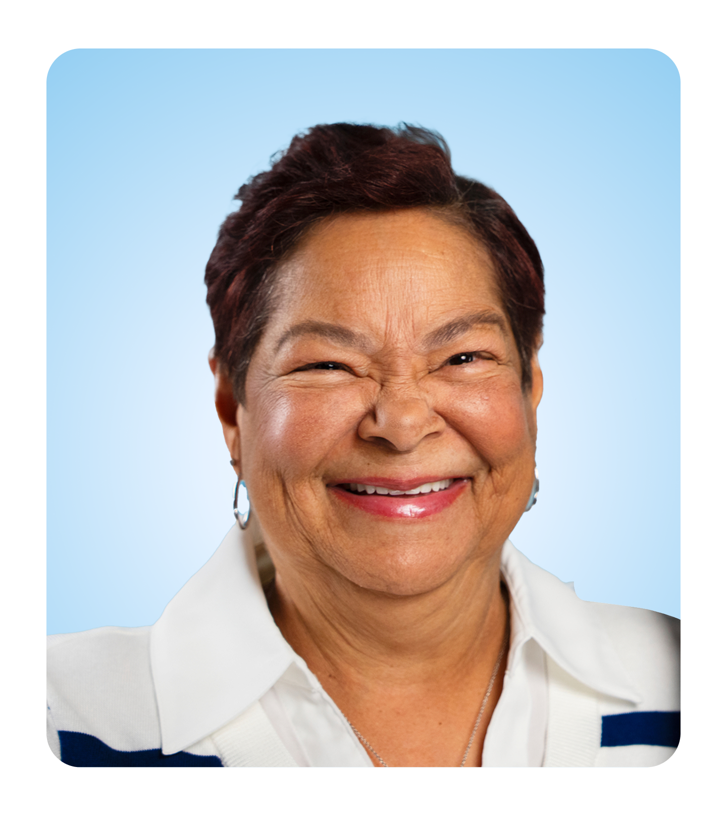 A person with short, dark hair wearing a white collared shirt with blue accents stands against a light blue background.