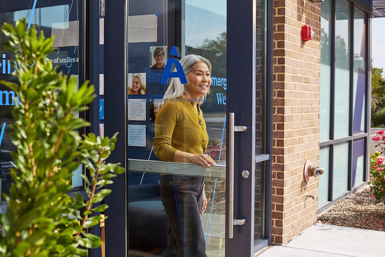 A smiling female patient exiting an Aspen Dental office through the front door.