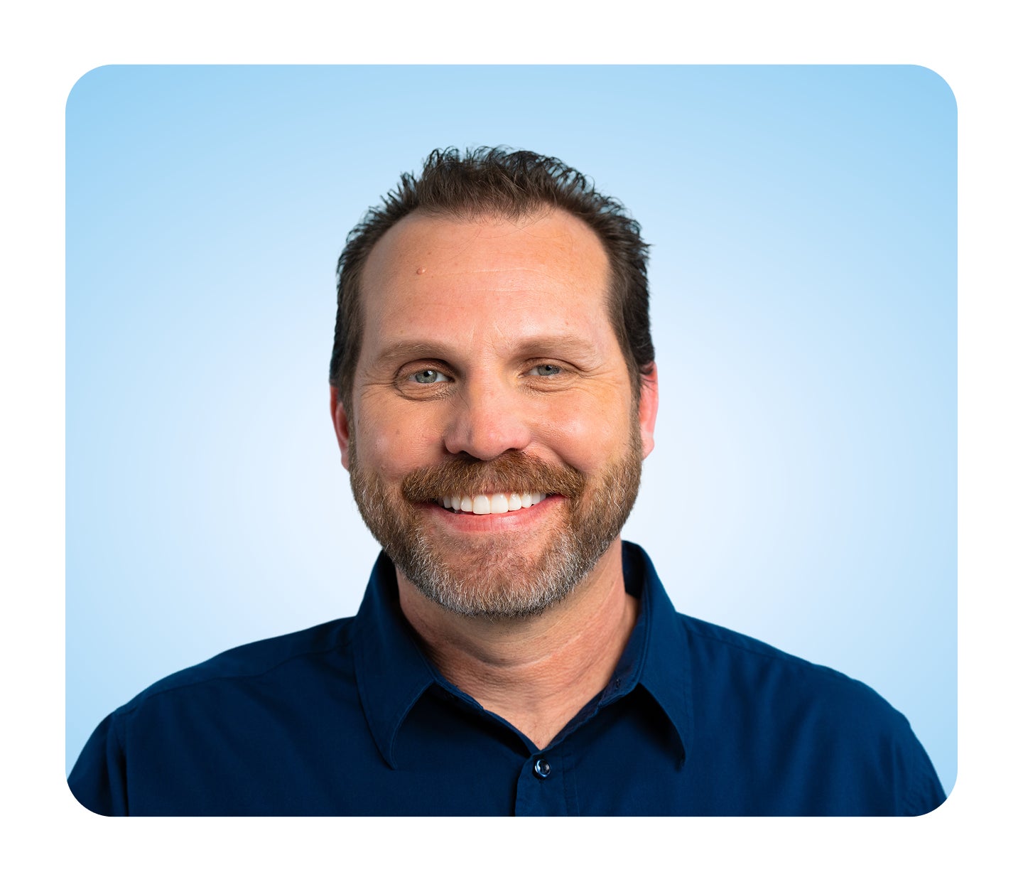 Portrait of a person wearing a dark blue collared shirt, standing against a light blue background.