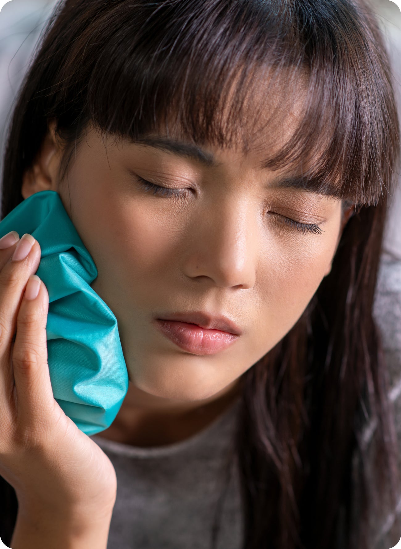 Woman holding an ice pack to her cheek with eyes closed, suggesting dental pain or a dental emergency before seeing a dentist.