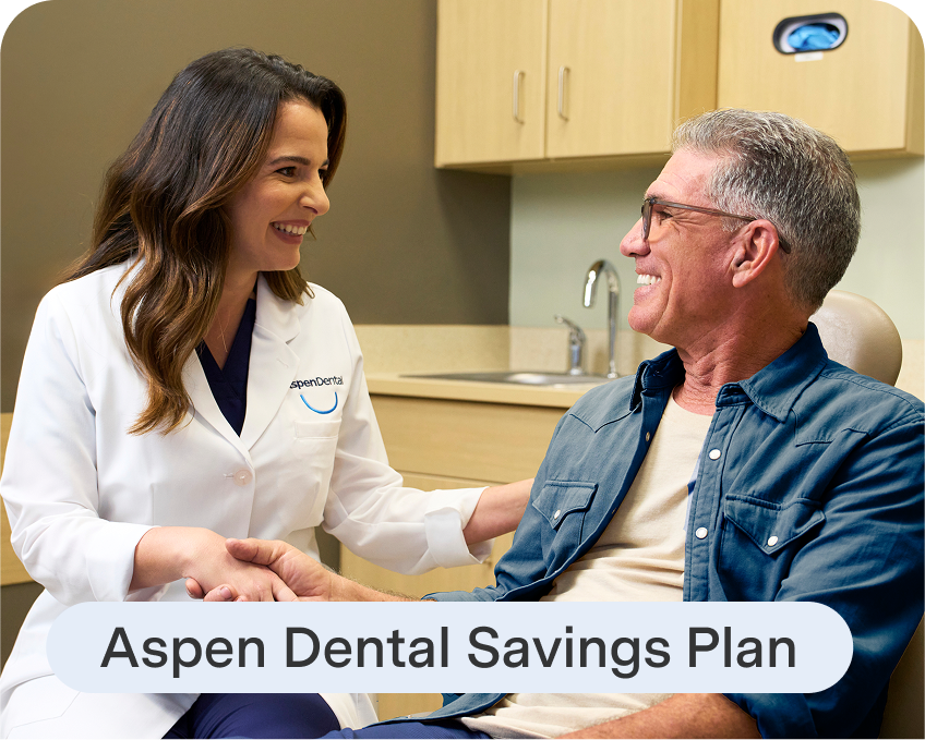 An Aspen Dental dentist smiles while speaking with a patient in the exam chair, with text reading “Aspen Dental Savings Plan” displayed below.