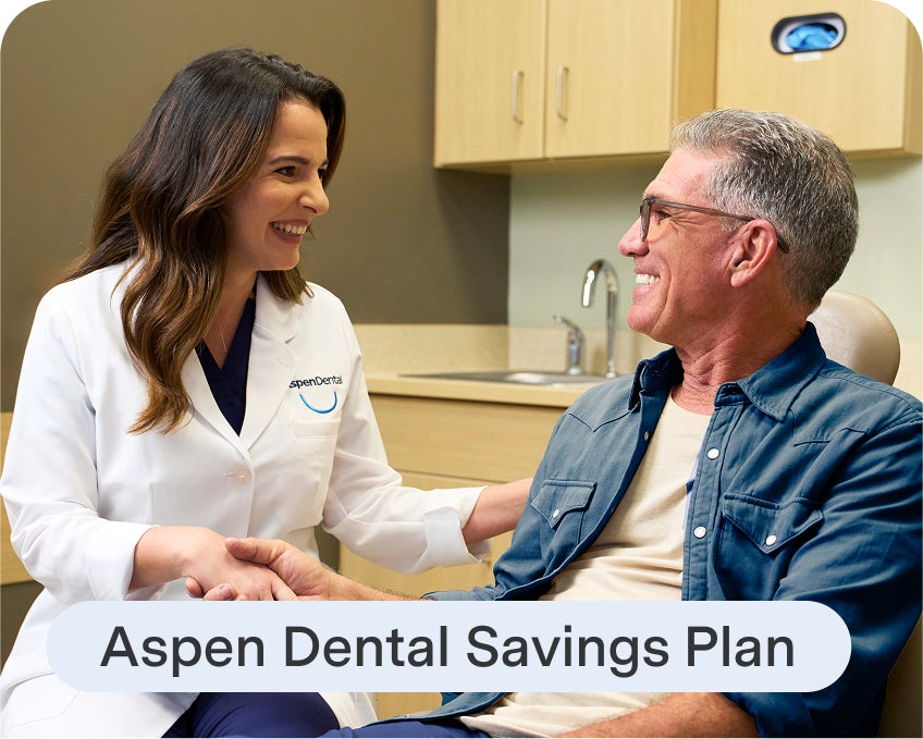 An Aspen Dental dentist smiles while speaking with a patient in the exam chair, with text reading “Aspen Dental Savings Plan” displayed below.