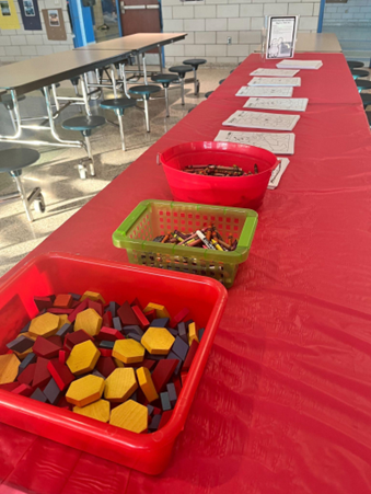 A long table covered with a red tablecloth holding bins of colorful plastic counters and classroom materials.