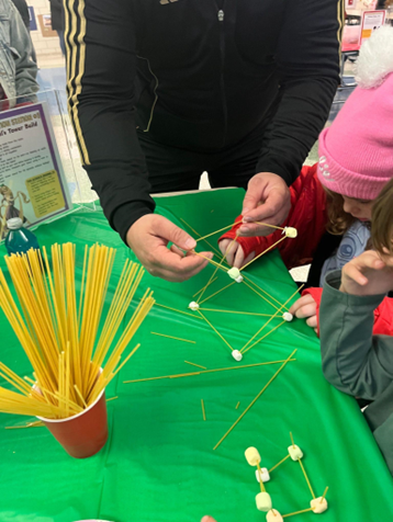 Students building a small structure using spaghetti sticks and marshmallows during a classroom activity.