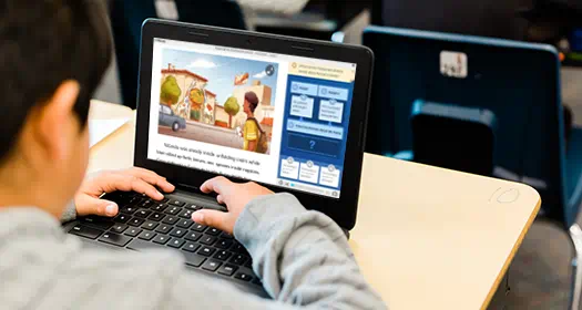 A student uses a laptop in a classroom, interacting with an educational program featuring a story and comprehension questions.