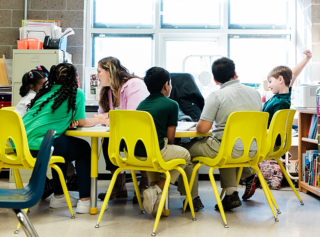  A group of students sitting at a table in yellow chairs during a small-group lesson.