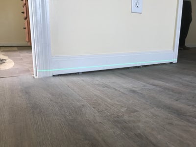 A home baseboard with a laser level across it indicating sagging floors