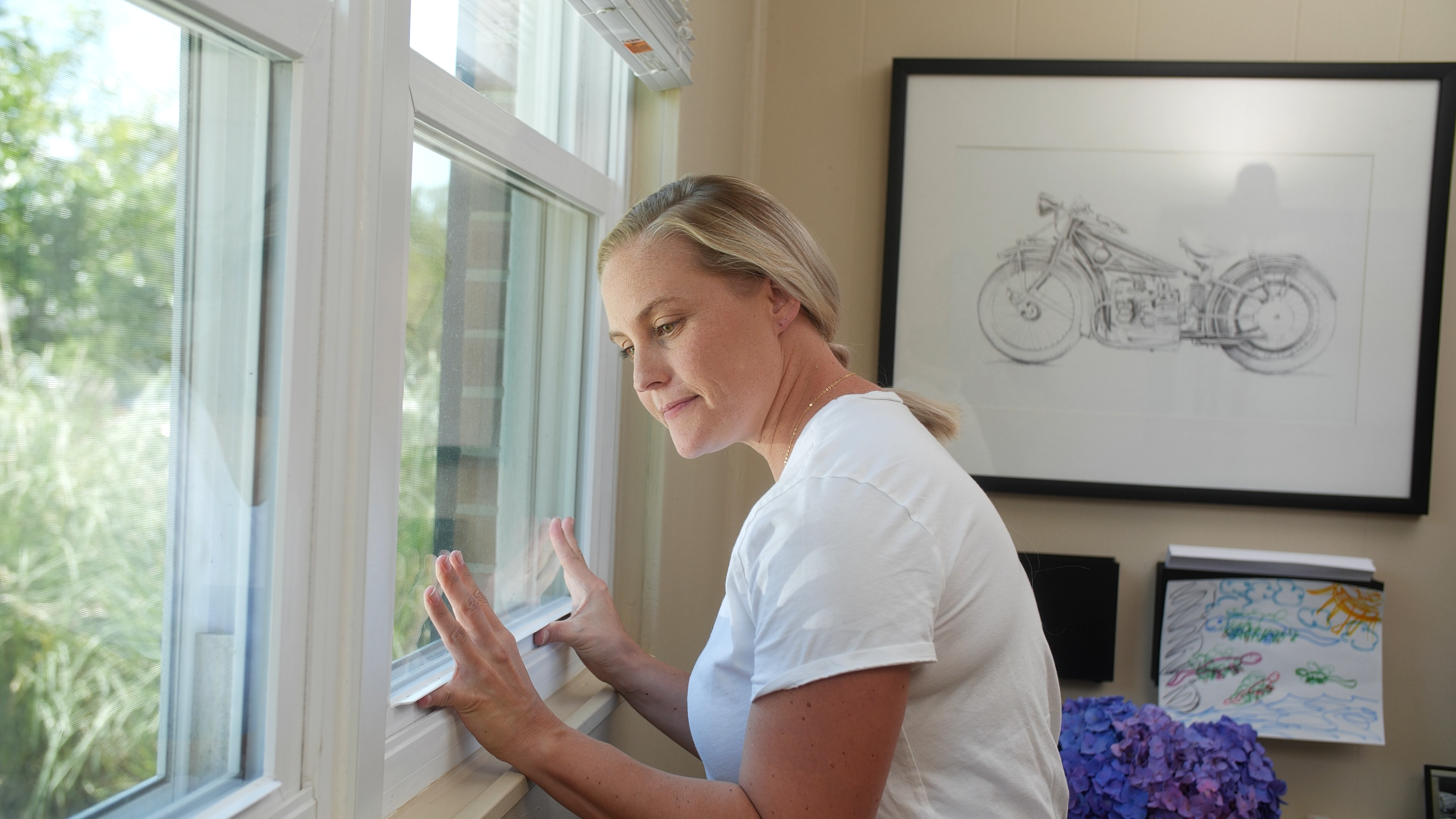 A women struggling to open her window because her foundation has shifted. Her window is misaligned and sticking 
