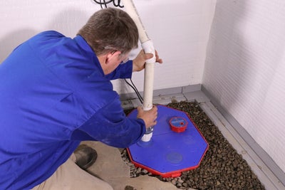 A Groundworks worker installing a sump pump system in a basement.