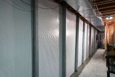 Basement wall with vapor barrier and steel support beams.